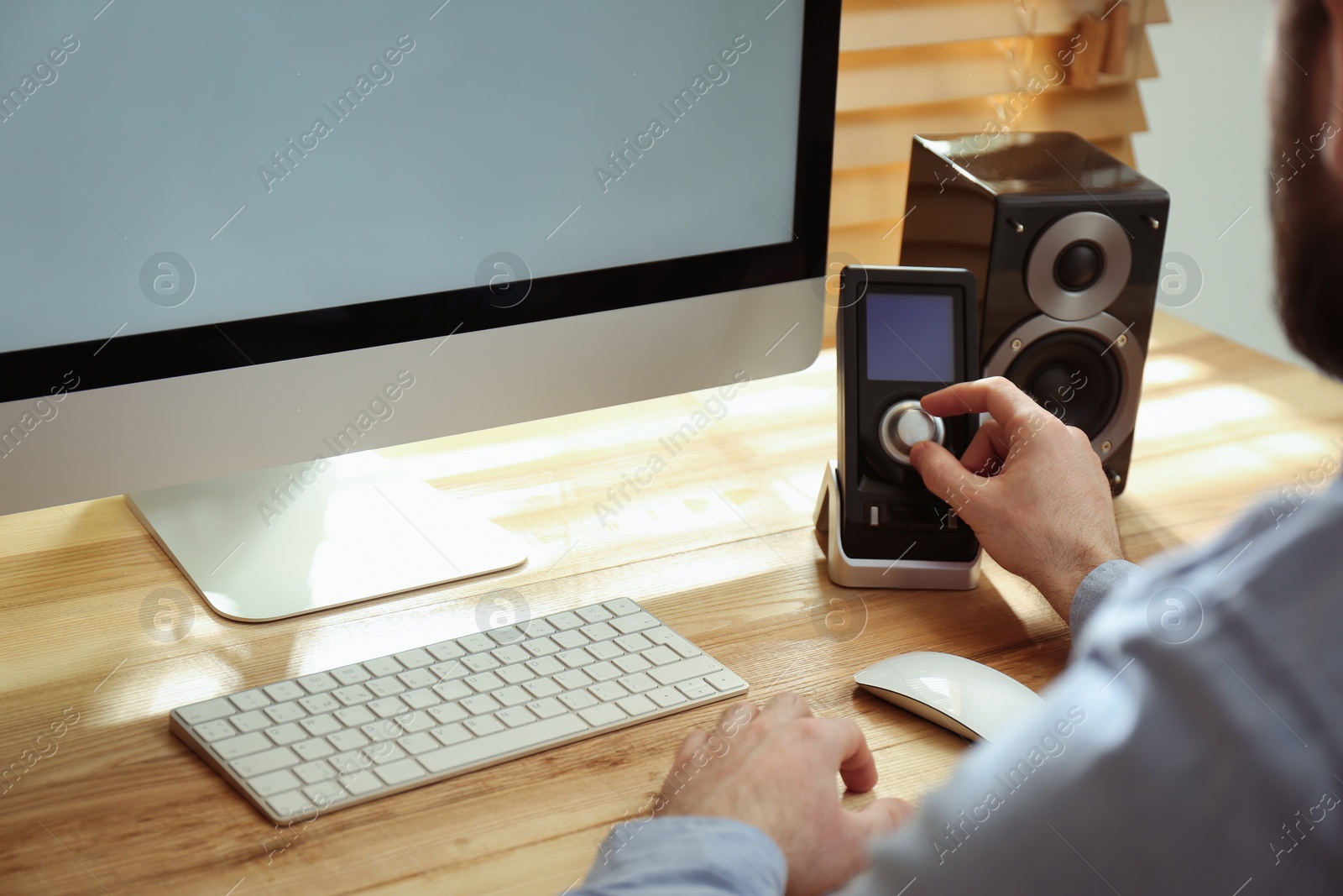 Photo of Man using remote to control audio speakers at table indoors, closeup