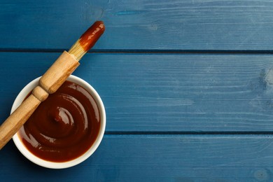 Photo of Tasty barbeque sauce in bowl and brush on blue wooden table, top view. Space for text