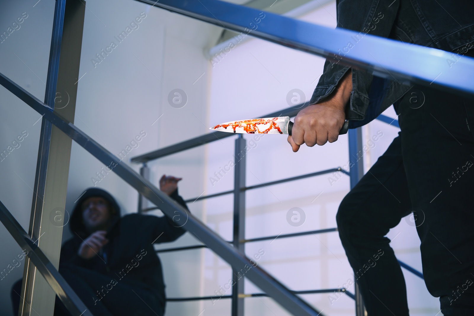 Photo of Criminal with knife attacking man on stairs indoors, closeup