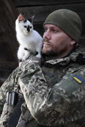 Photo of Ukrainian soldier rescuing animal. Little stray cat on man's shoulder, closeup
