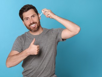 Man using ear spray and showing thumbs up on light blue background, space for text