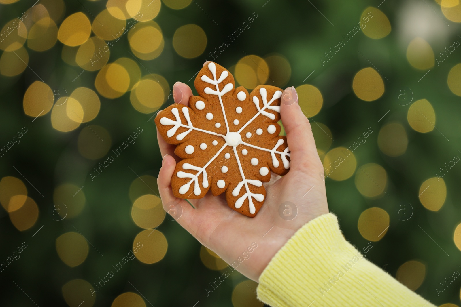 Photo of Woman with decorated cookie against blurred Christmas lights, closeup