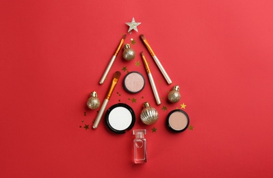 Photo of Christmas tree shape of decorative cosmetic products on red background, flat lay. Winter care