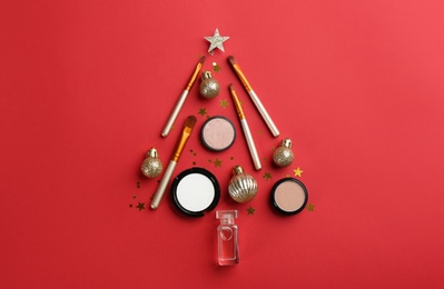 Christmas tree shape of decorative cosmetic products on red background, flat lay. Winter care