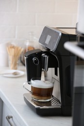 Photo of Modern coffee machine with glass cup of latte on white marble countertop in kitchen