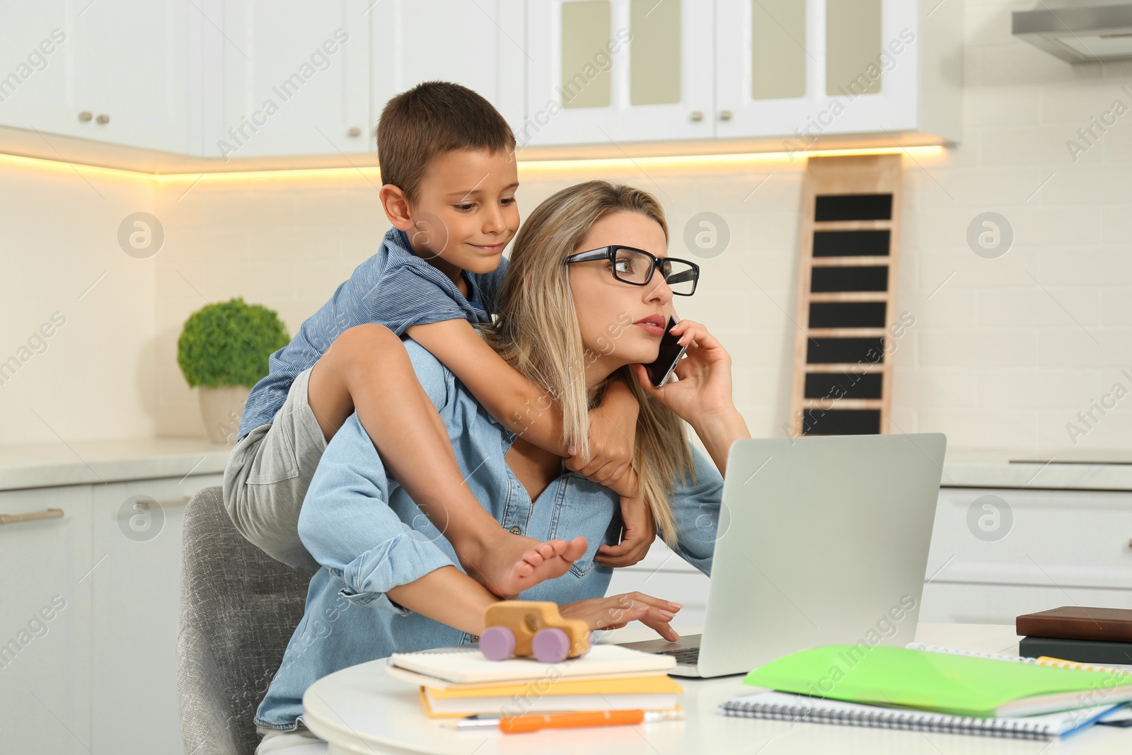 Photo of Little boy bothering mother at work in kitchen. Home office concept