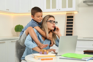 Little boy bothering mother at work in kitchen. Home office concept