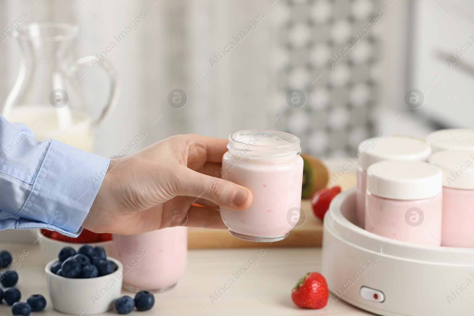 Photo of Woman making tasty yogurt at white wooden table in kitchen, closeup