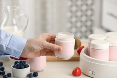 Woman making tasty yogurt at white wooden table in kitchen, closeup