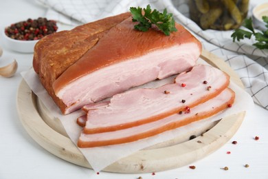 Photo of Delicious smoked bacon with parsley and peppercorns on white table