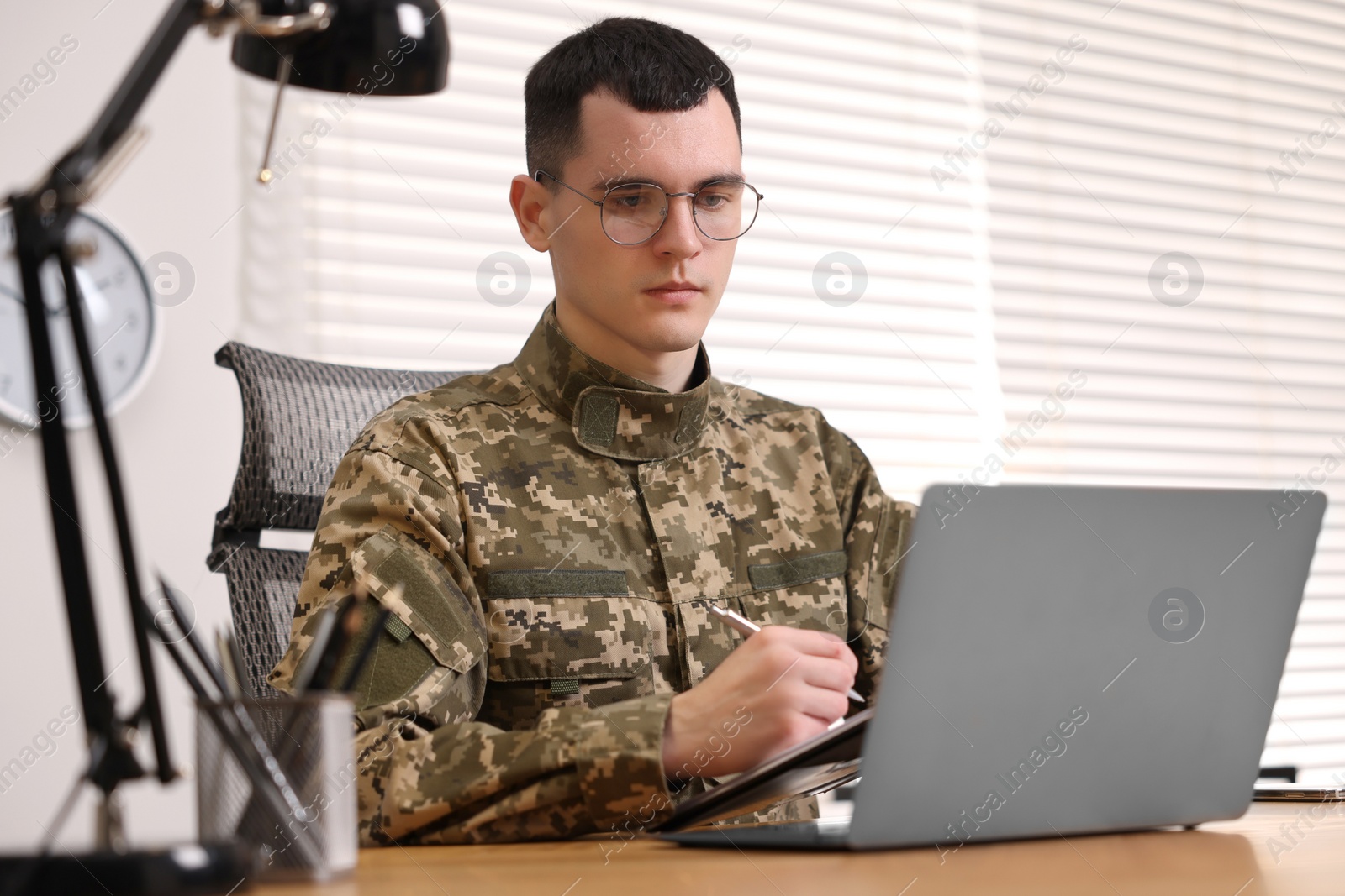 Photo of Military service. Young soldier working at table in office