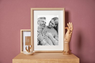 Black and white family portrait of man and woman in photo frame on table near color wall