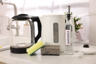 Photo of Cleaning electric kettle. Bottle of vinegar, sponges and baking soda on countertop in kitchen