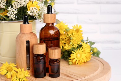 Photo of Bottles of essential oil and different wildflowers on wooden board, space for text