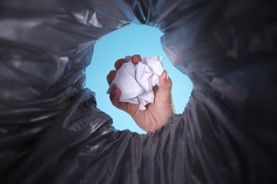 Photo of Bottom view of woman throwing crumpled paper into trash bin on light blue background, closeup