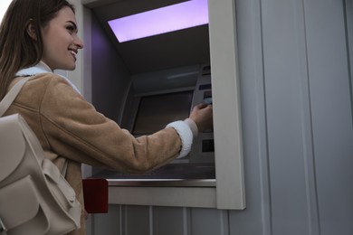 Young woman using cash machine for money withdrawal outdoors