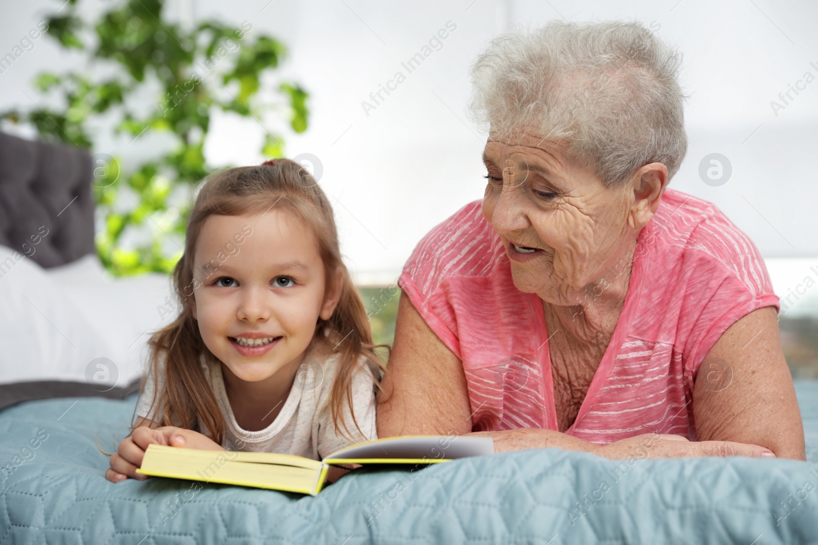 Photo of Cute girl and her grandmother reading book on bed at home