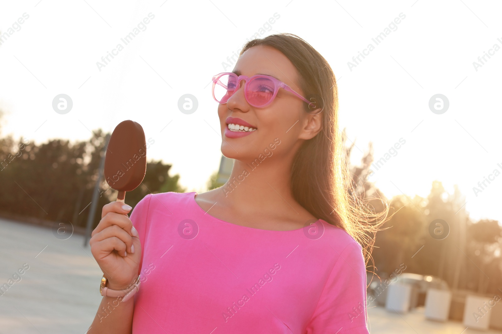 Photo of Beautiful young woman holding ice cream glazed in chocolate on city street