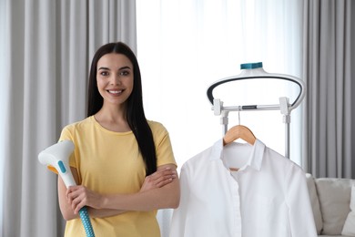 Happy woman with steam iron and white shirt at home