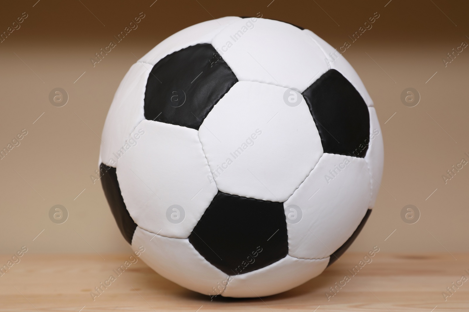 Photo of Soccer ball on wooden table near beige wall. Sports equipment