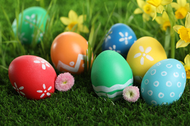 Photo of Colorful Easter eggs and flowers in green grass, closeup