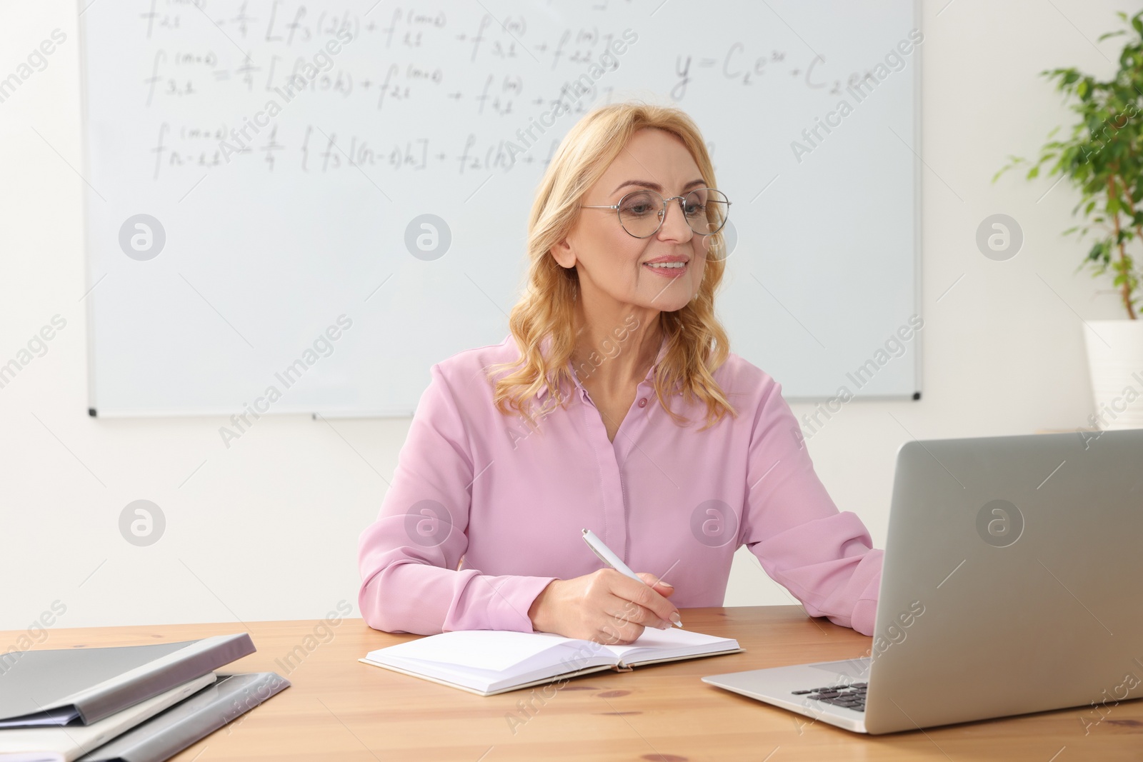 Photo of Teacher giving lesson near laptop at desk in classroom