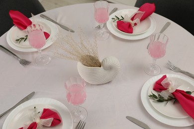 Photo of Color accent table setting. Glasses, plates, cutlery and pink napkins on table