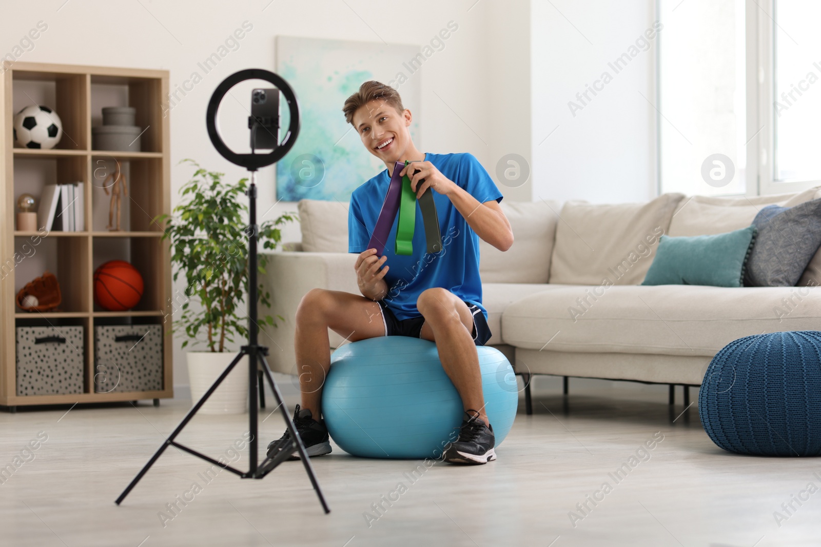 Photo of Smiling sports blogger with resistance bands streaming online fitness lesson at home