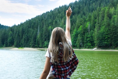 Woman near clear lake in green forest at summer, back view