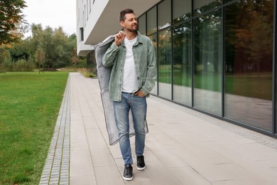 Photo of Attractive happy man holding garment cover with clothes outdoors. Dry cleaning service