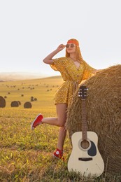 Happy hippie woman with guitar near hay bale outdoors
