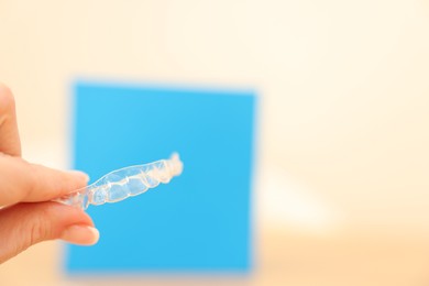 Photo of Woman with transparent dental aligner on blurred background, closeup. Space for text