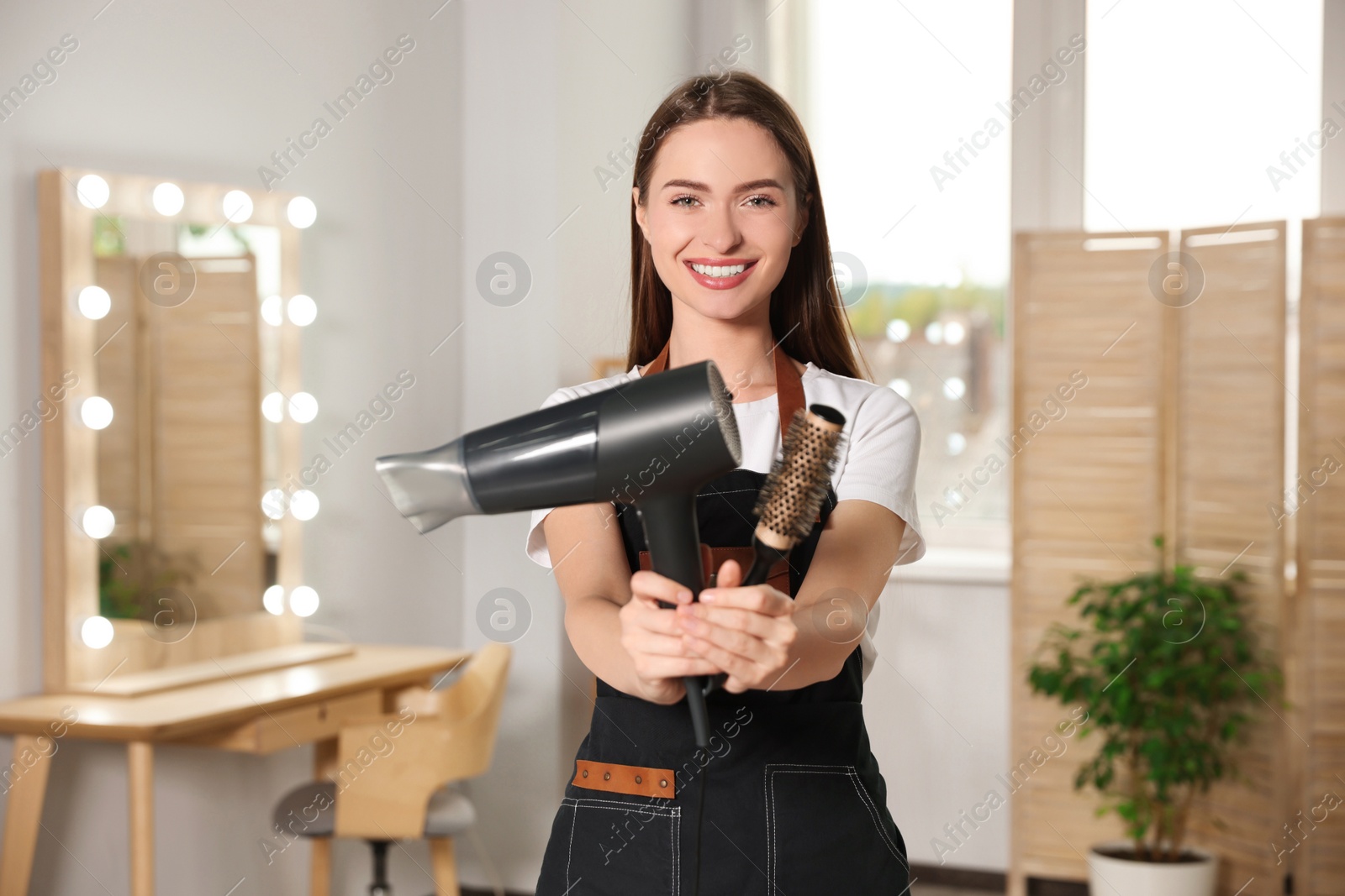 Photo of Portrait of happy hairdresser with hairdryer and brush in beauty salon