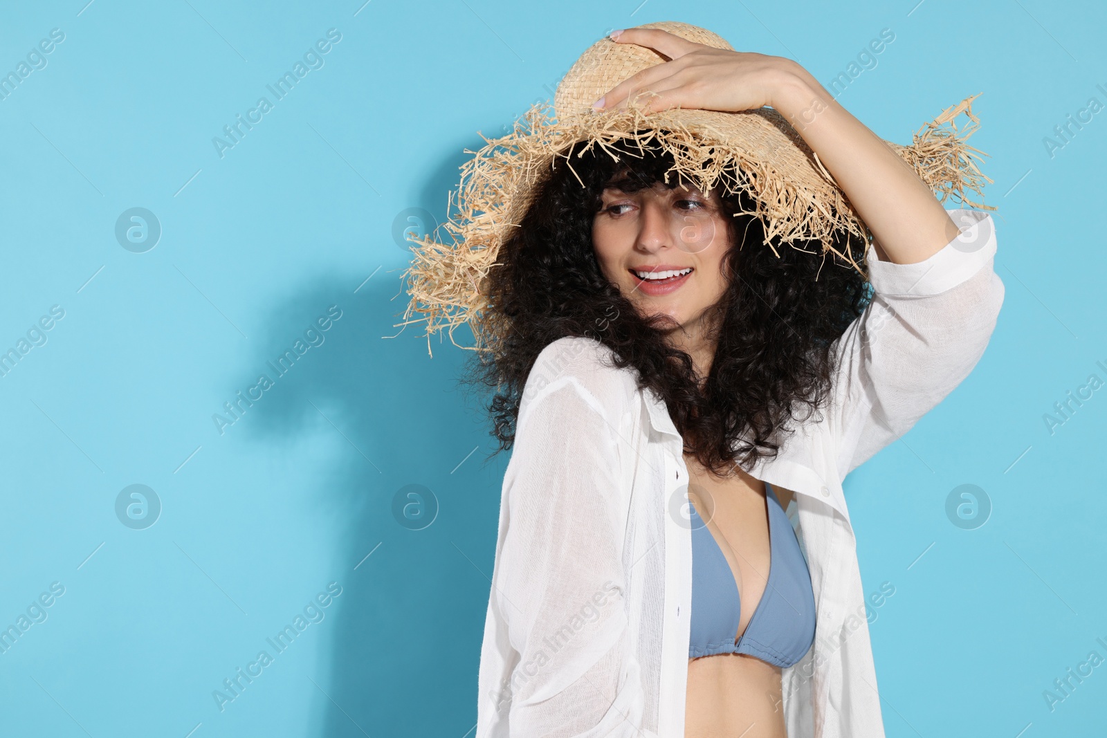 Photo of Beautiful young woman wearing straw hat on light blue background, space for text. Sun protection accessory