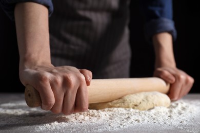 Making bread. Woman rolling dough at table on dark background, closeup