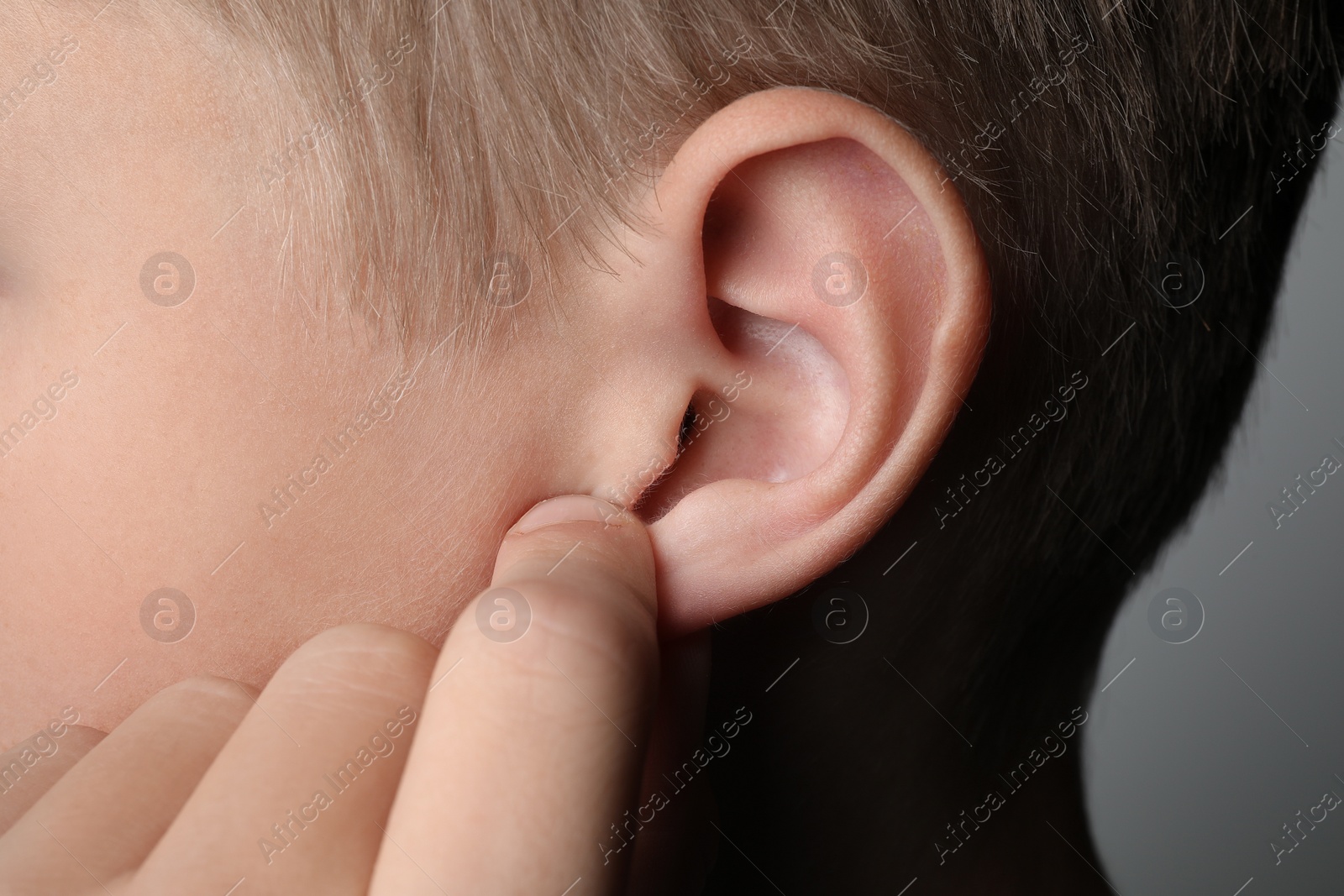 Photo of Boy touching his ear on grey background, closeup