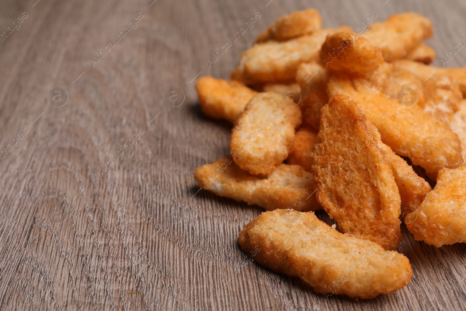 Photo of Heap of crispy rusks on wooden table, closeup. Space for text