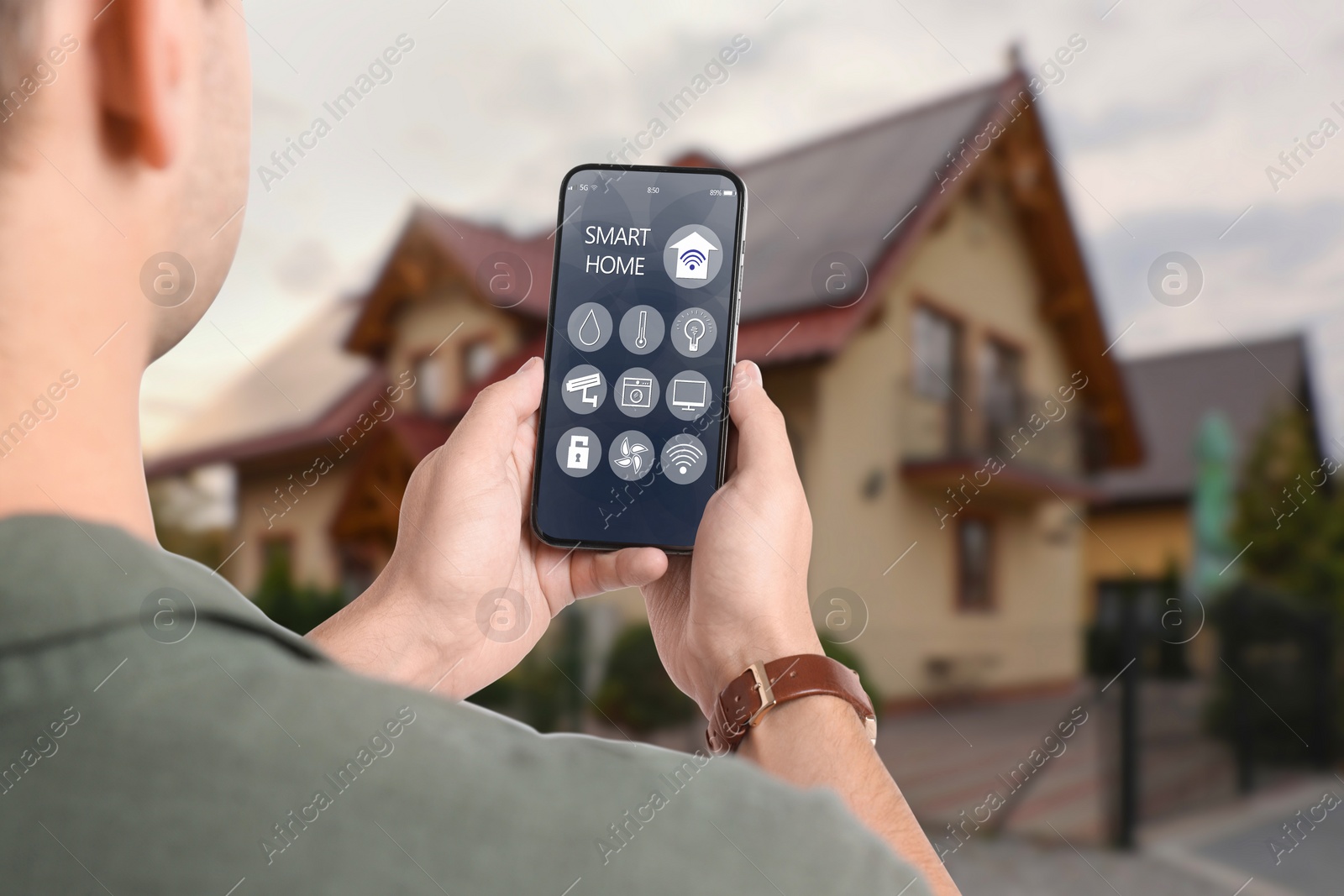 Image of Man using smart home control system via mobile phone near house outdoors, closeup