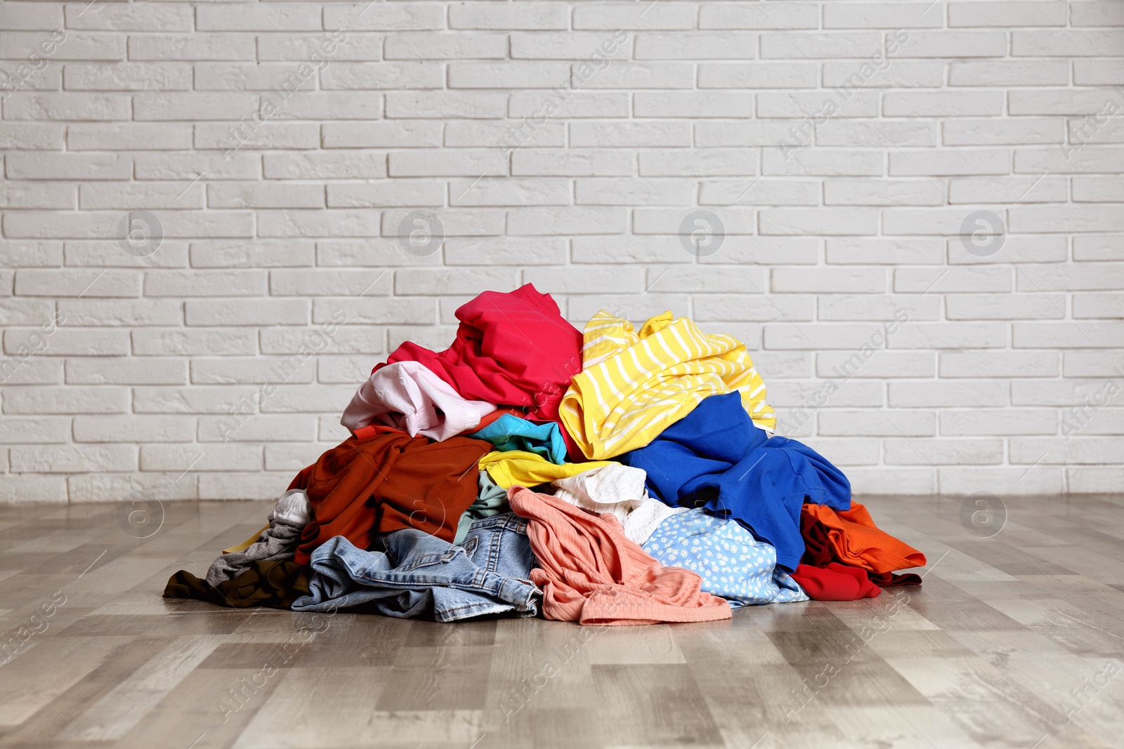 Photo of Pile of dirty clothes on floor near brick wall