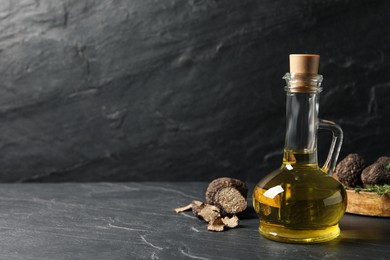 Fresh truffle oil in glass jug on black table, space for text