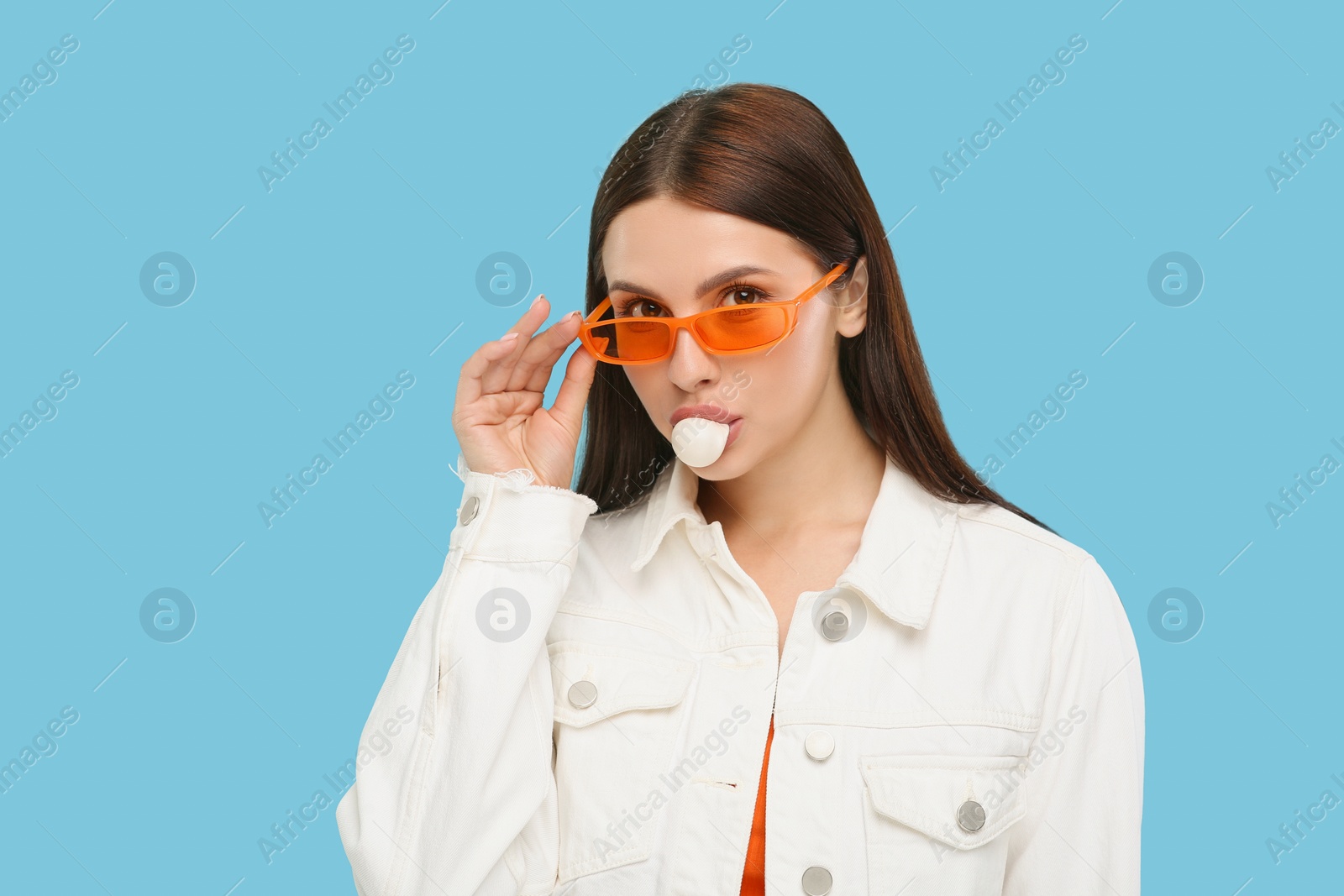 Photo of Beautiful woman in sunglasses blowing bubble gum on light blue background