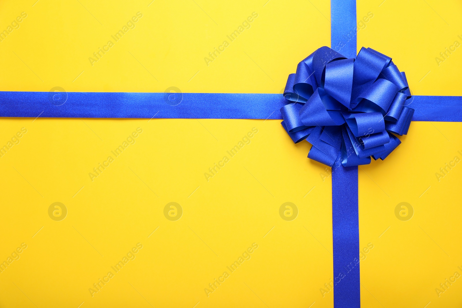 Photo of Blue ribbons with bow on yellow background, top view. Space for text