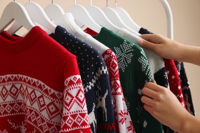 Photo of Woman choosing Christmas sweater from rack, closeup