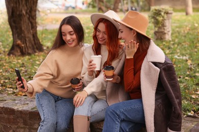 Photo of Happy friends with paper cups of coffee taking selfie in park