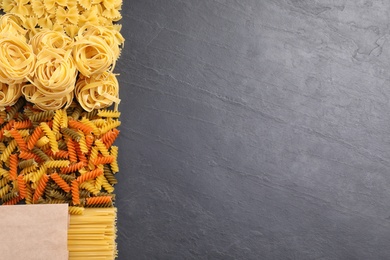 Photo of Different types of pasta on grey table, flat lay. Space for text