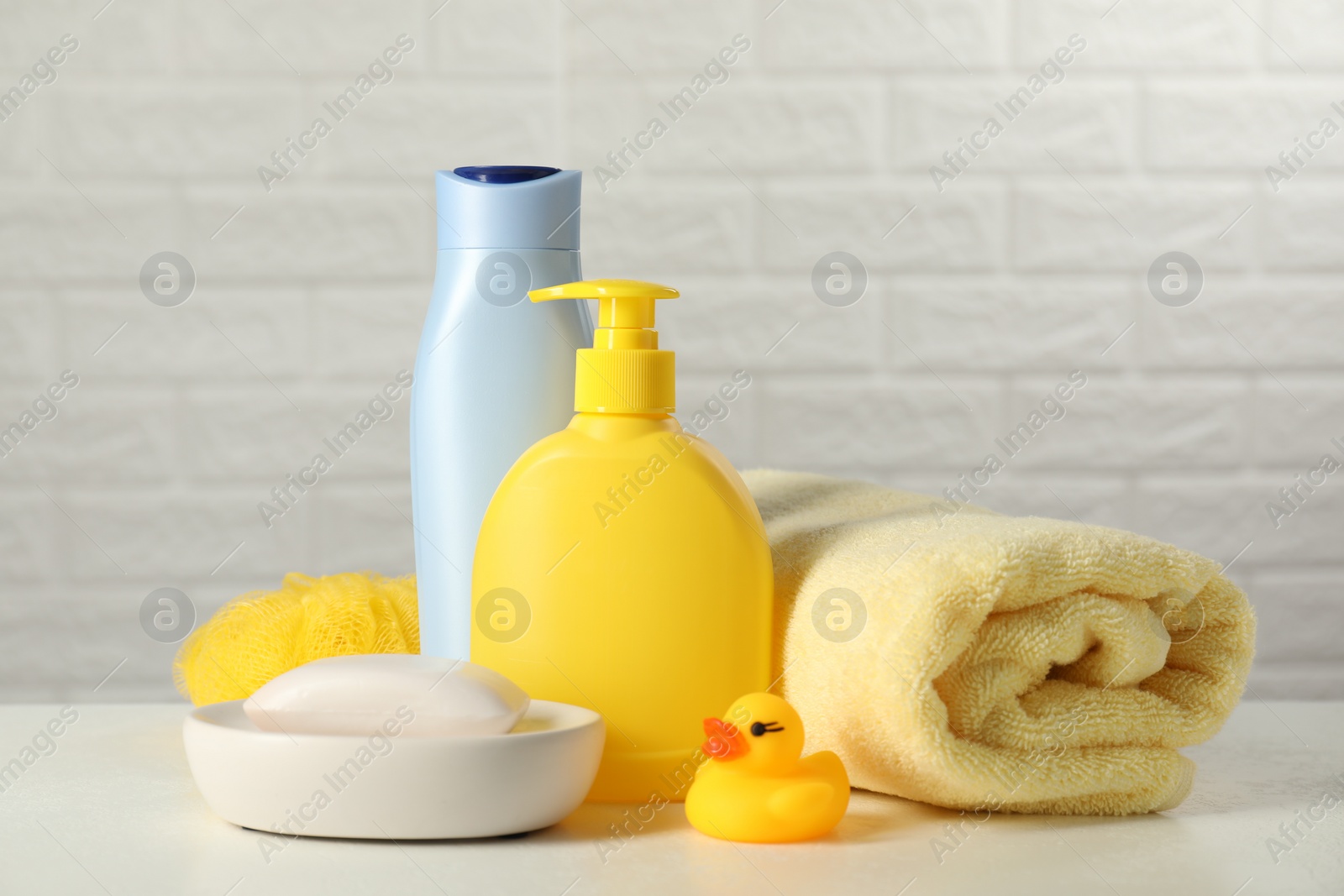 Photo of Baby cosmetic products, bath duck, sponge and towel on white table against brick wall