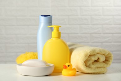 Baby cosmetic products, bath duck, sponge and towel on white table against brick wall