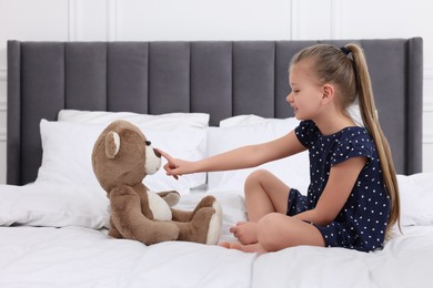 Cute little girl playing with teddy bear on bed