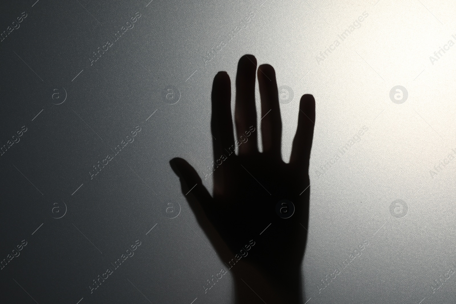 Photo of Silhouette of creepy ghost behind glass against grey background, closeup