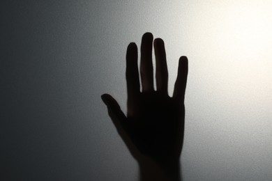 Photo of Silhouette of creepy ghost behind glass against grey background, closeup